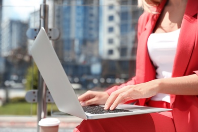 Photo of Businesswoman using laptop on city street, closeup