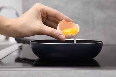 Photo of Woman adding raw egg into frying pan indoors, closeup