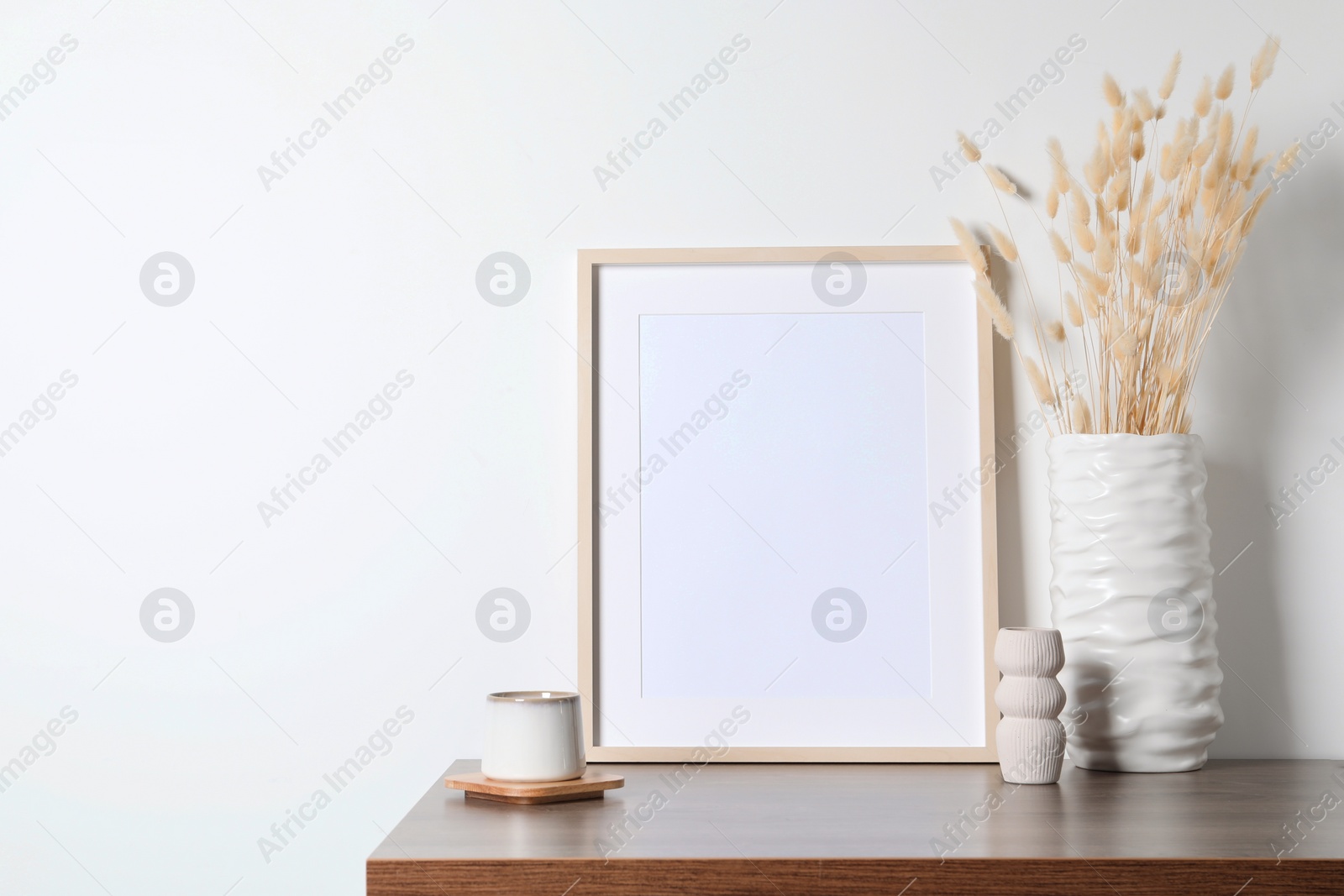 Photo of Empty photo frame, cup and vase with dry decorative spikes on wooden table. Mockup for design
