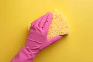Photo of Cleaner in rubber glove holding new sponge on yellow background, top view
