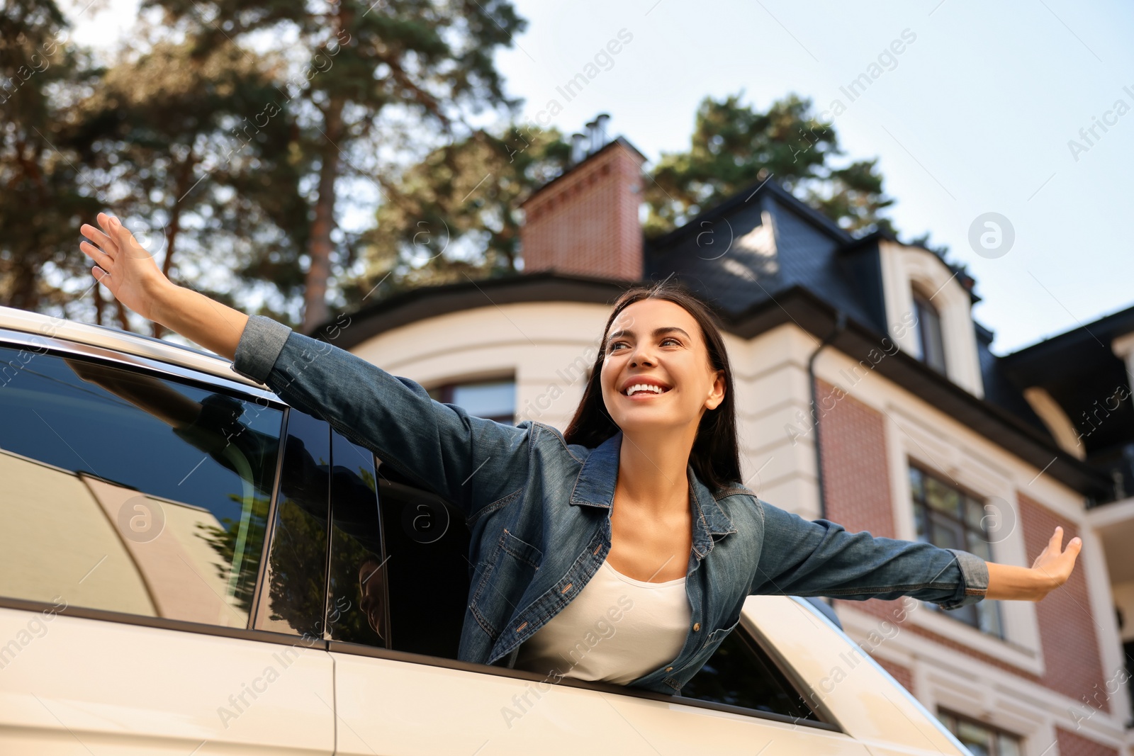 Photo of Enjoying trip. Happy young woman leaning out of car window on city street, low angle view