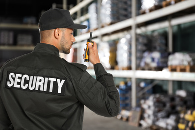 Image of Security guard using portable radio transmitter in wholesale warehouse, space for text