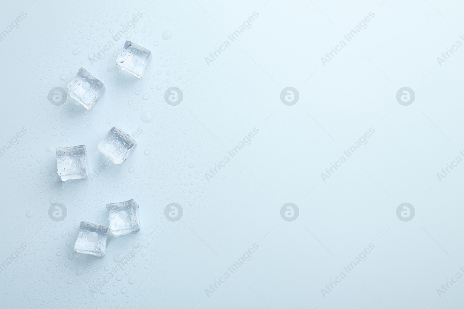 Photo of Crystal clear ice cubes on light blue background, flat lay. Space for text