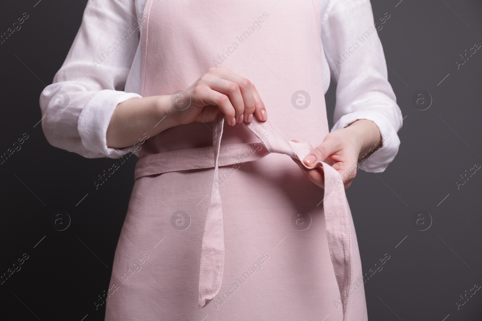 Photo of Woman putting on pink apron against grey background, closeup