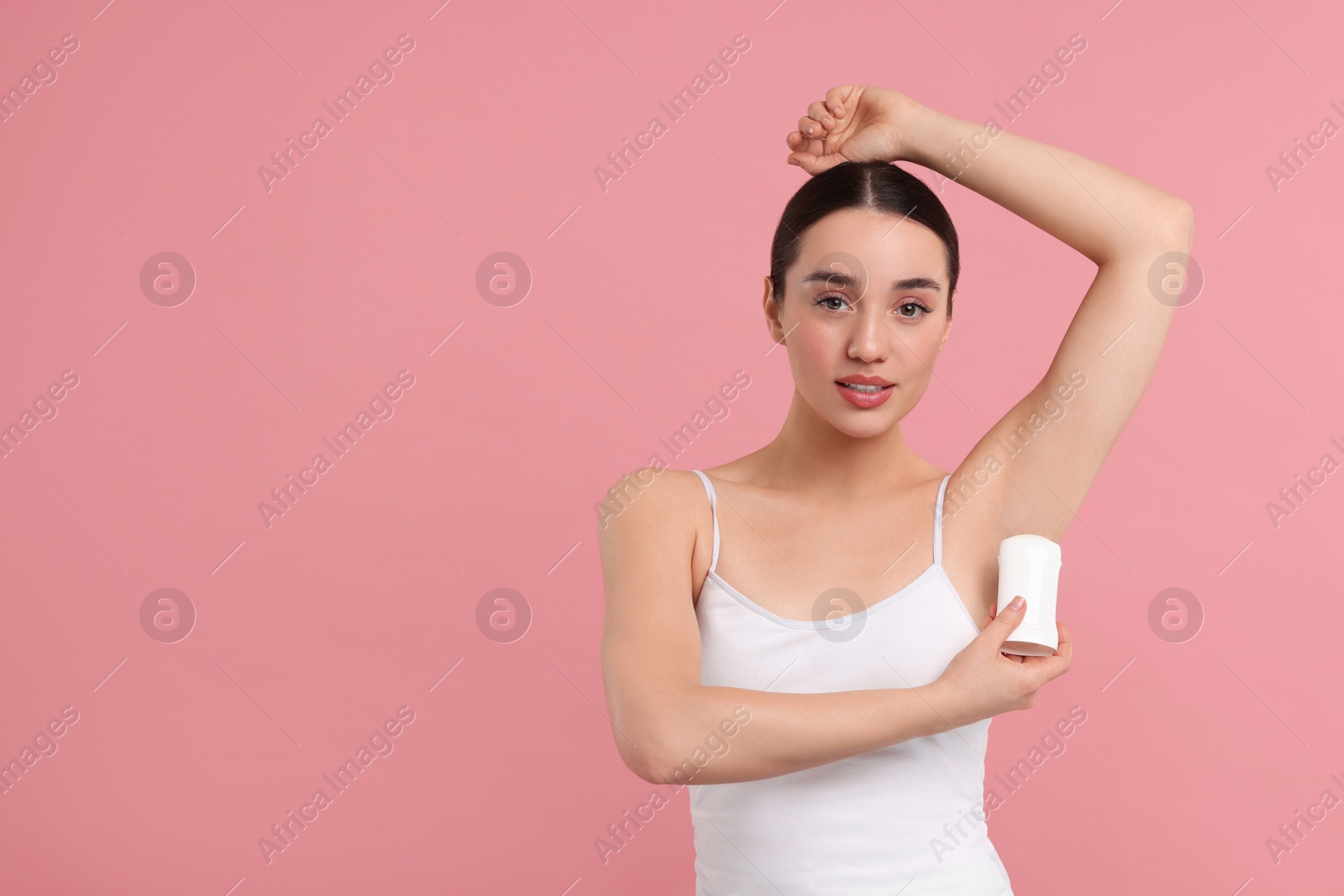 Photo of Beautiful woman applying deodorant on pink background, space for text