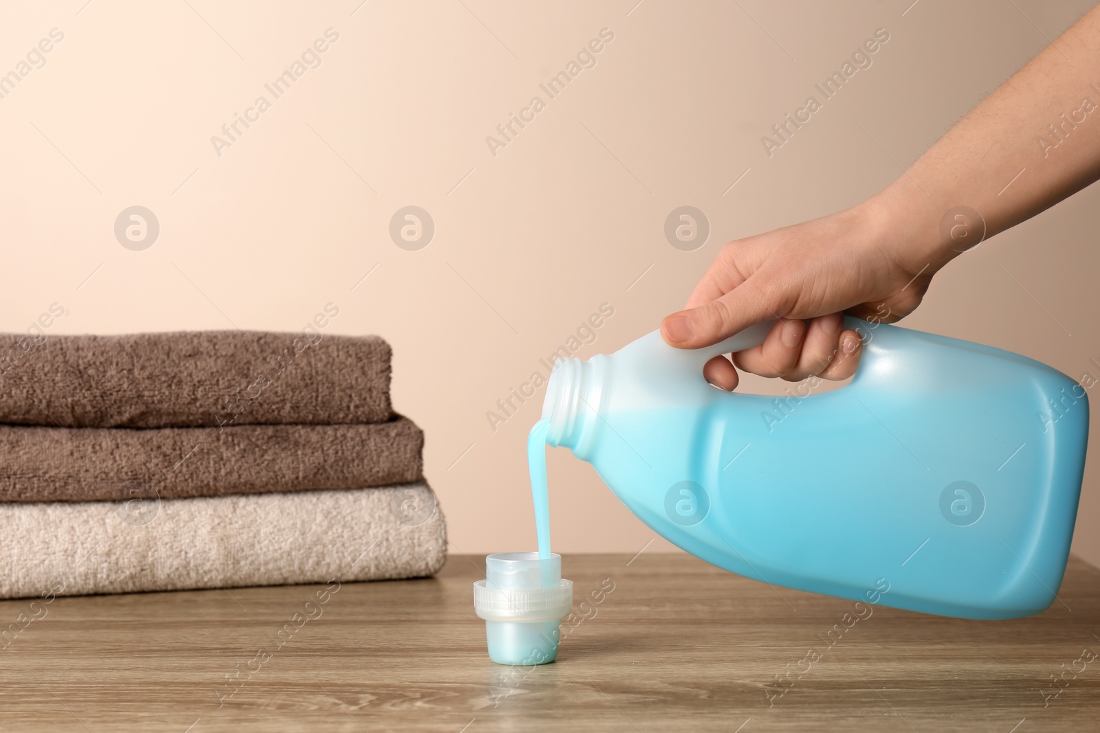 Photo of Woman pouring detergent into cap on table against color background, closeup. Laundry day