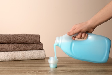 Photo of Woman pouring detergent into cap on table against color background, closeup. Laundry day