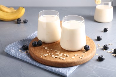 Photo of Tasty yogurt in glasses, oats and blueberries on grey table