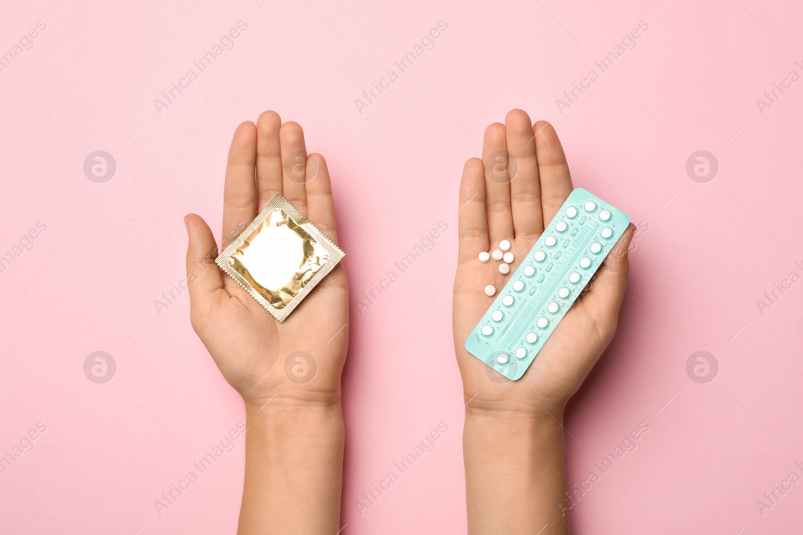 Photo of Woman holding condom and birth control pills on pink background, top view. Safe sex