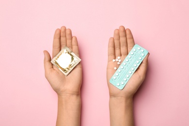 Woman holding condom and birth control pills on pink background, top view. Safe sex