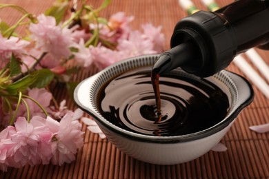 Pouring soy sauce into bowl and beautiful blossoming branch on bamboo mat, closeup