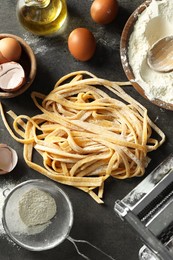 Homemade pasta, maker and ingredients on dark grey table, flat lay