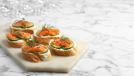 Tasty canapes with salmon, cucumber and cream cheese on white marble table. Space for text
