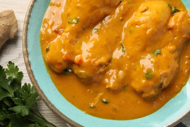 Photo of Tasty chicken curry, parsley and ginger on wooden table, flat lay