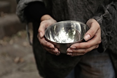 Photo of Poor homeless woman with empty bowl outdoors, closeup