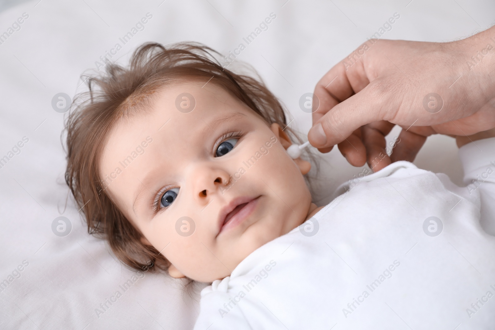 Photo of Father cleaning ear of his baby with cotton bud on bed, closeup