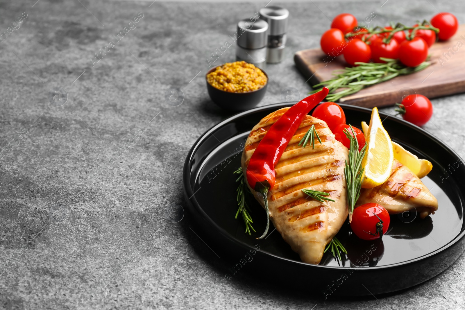 Photo of Tasty grilled chicken fillets with lemon, chili pepper and rosemary on grey table. Space for text