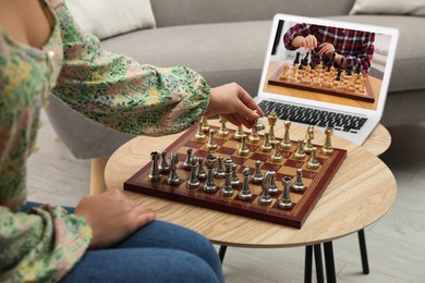 Image of Woman playing chess with partner via online video chat in living room, closeup