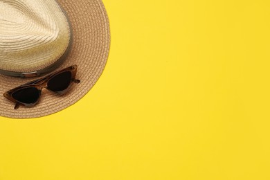 Hat and sunglasses on yellow background, flat lay with space for text. Sun protection