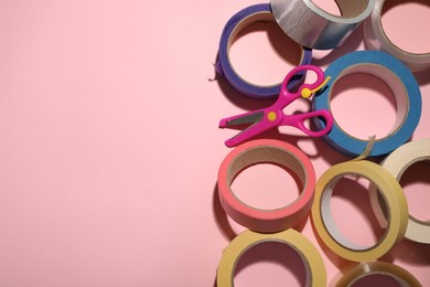 Photo of Many rolls of adhesive tape and scissors on pink background, flat lay. Space for text