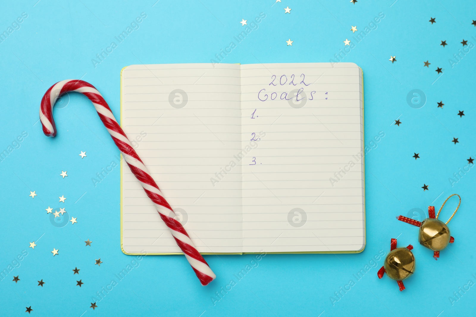 Photo of Open planner, confetti, candy cane and bells on light blue background, flat lay. Planning for 2022 New Year