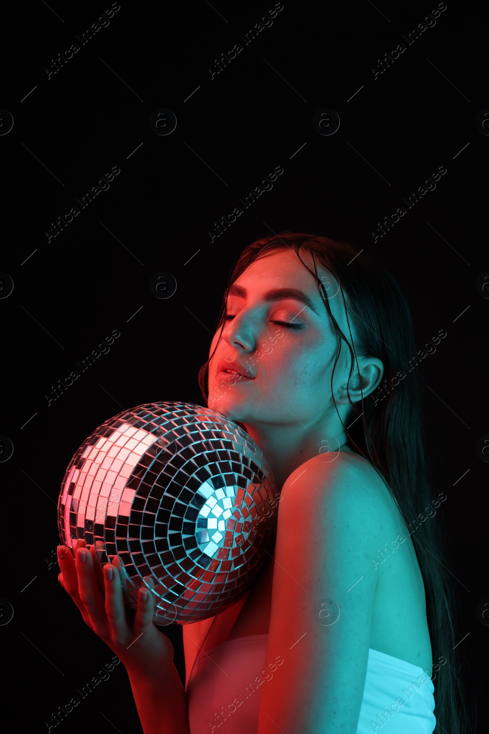 Photo of Beautiful woman with disco ball posing in neon lights against black background