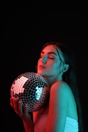 Photo of Beautiful woman with disco ball posing in neon lights against black background