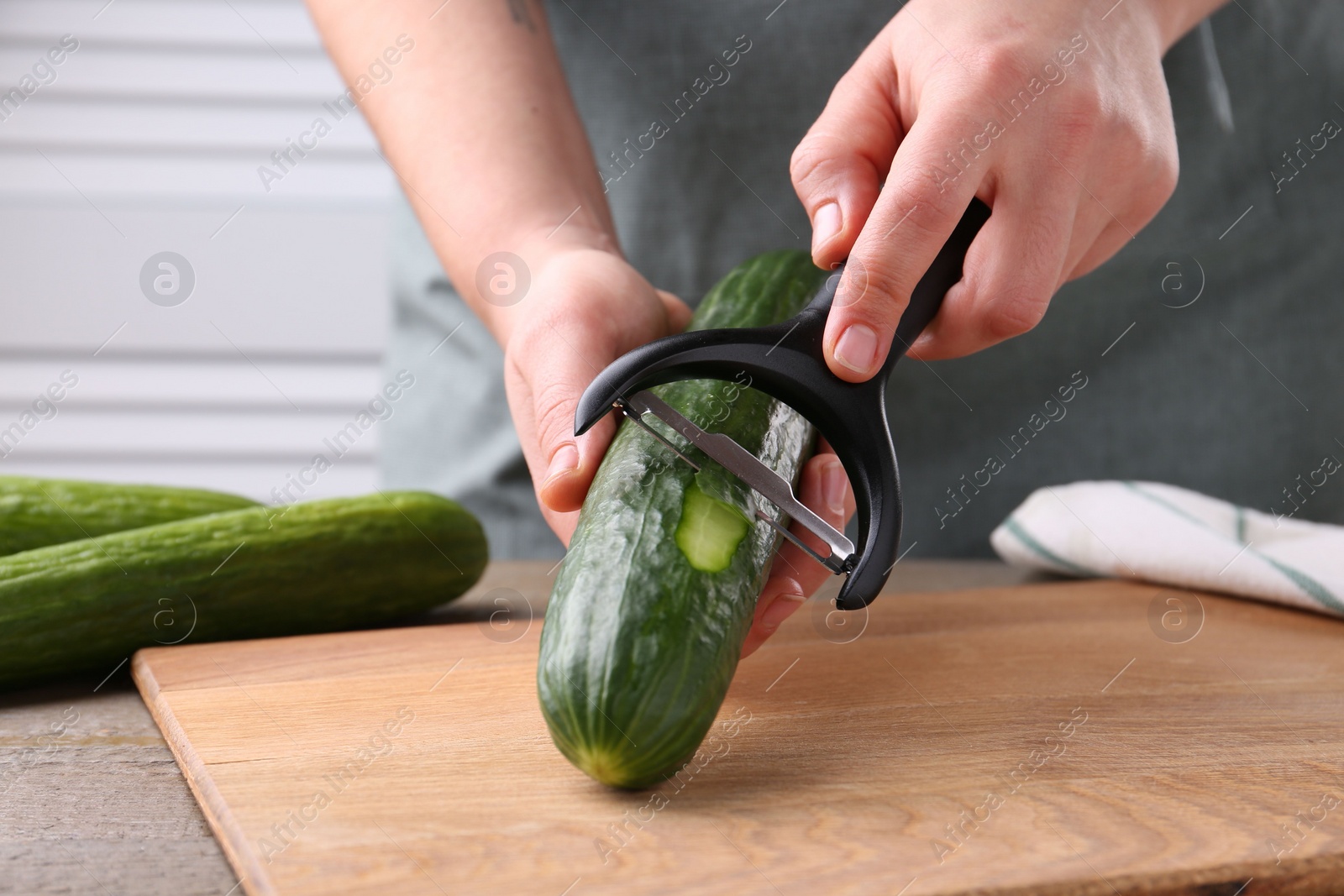 Photo of Woman peeling cucumber at wooden table indoors, closeup