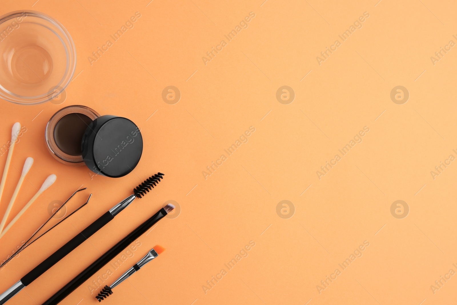 Photo of Eyebrow pomade with henna effect and professional tools on orange background, flat lay. Space for text