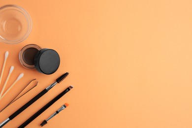 Eyebrow pomade with henna effect and professional tools on orange background, flat lay. Space for text