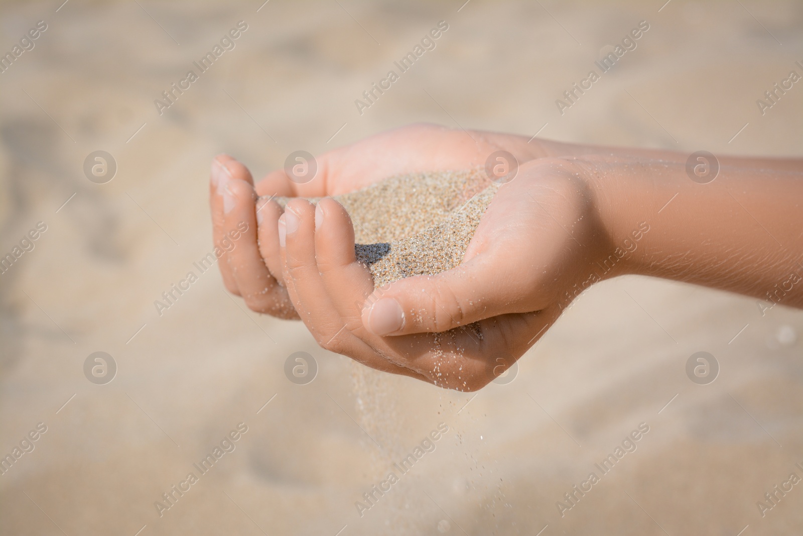 Photo of Child pouring sand from hands outdoors, closeup. Fleeting time concept