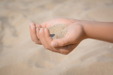 Photo of Child pouring sand from hands outdoors, closeup. Fleeting time concept