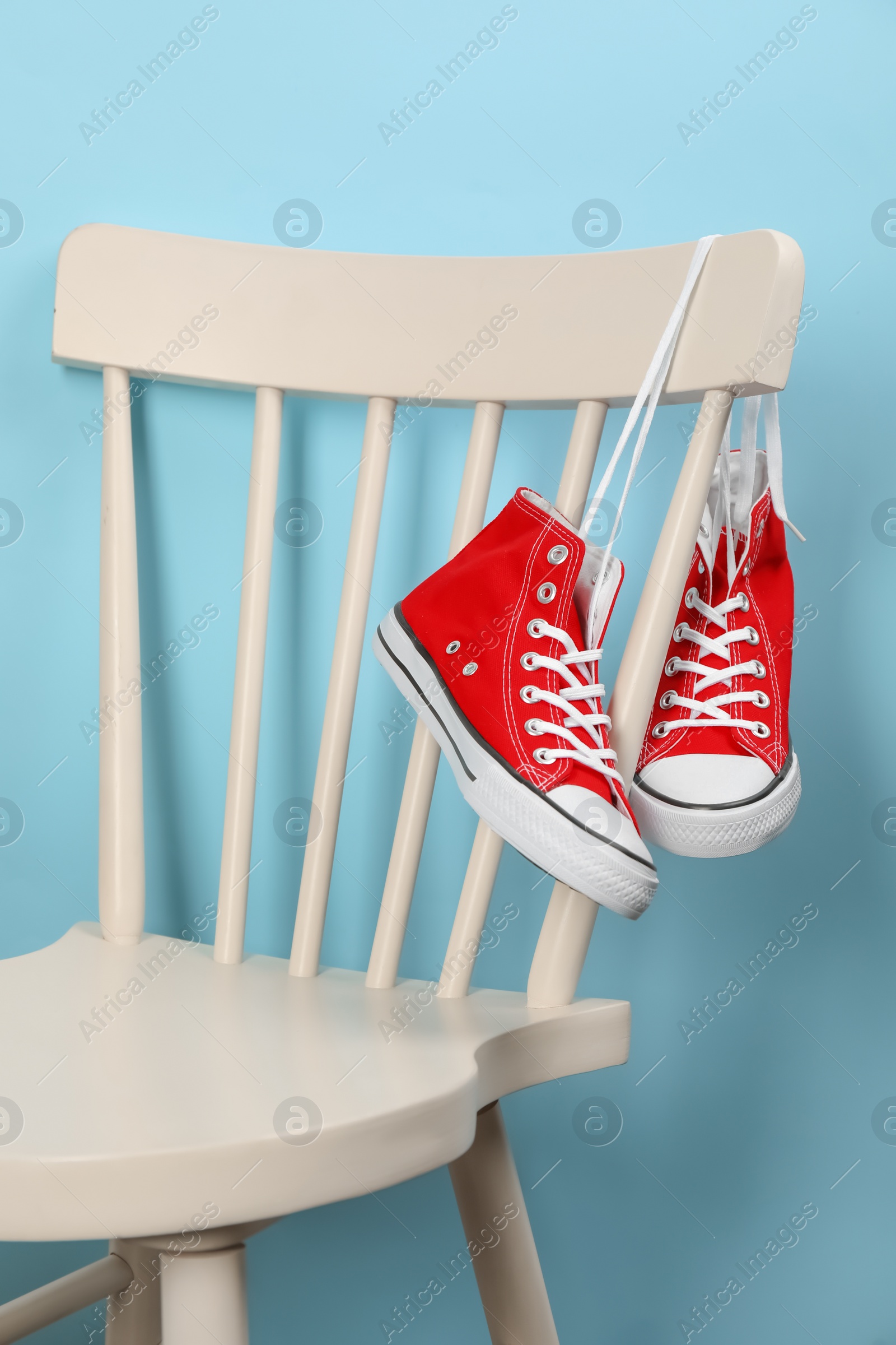 Photo of Pair of sneakers hanging on chair near light blue wall