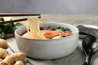 Photo of Eating delicious ramen from bowl with chopsticks at table, closeup. Noodle soup