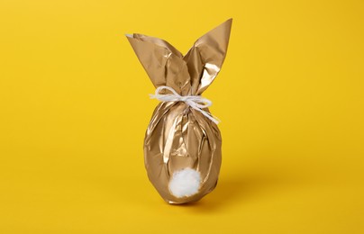 Easter bunny made of shiny gold paper and egg on yellow background