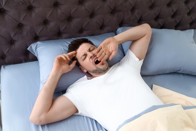 Photo of Handsome man yawning while lying on pillow, view from above. Bedtime