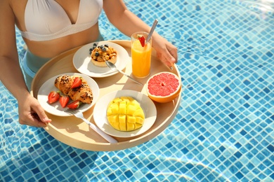 Young woman with delicious breakfast on floating tray in swimming pool, closeup