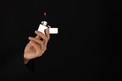 Photo of Woman holding lighter with burning flame on black background, closeup. Space for text