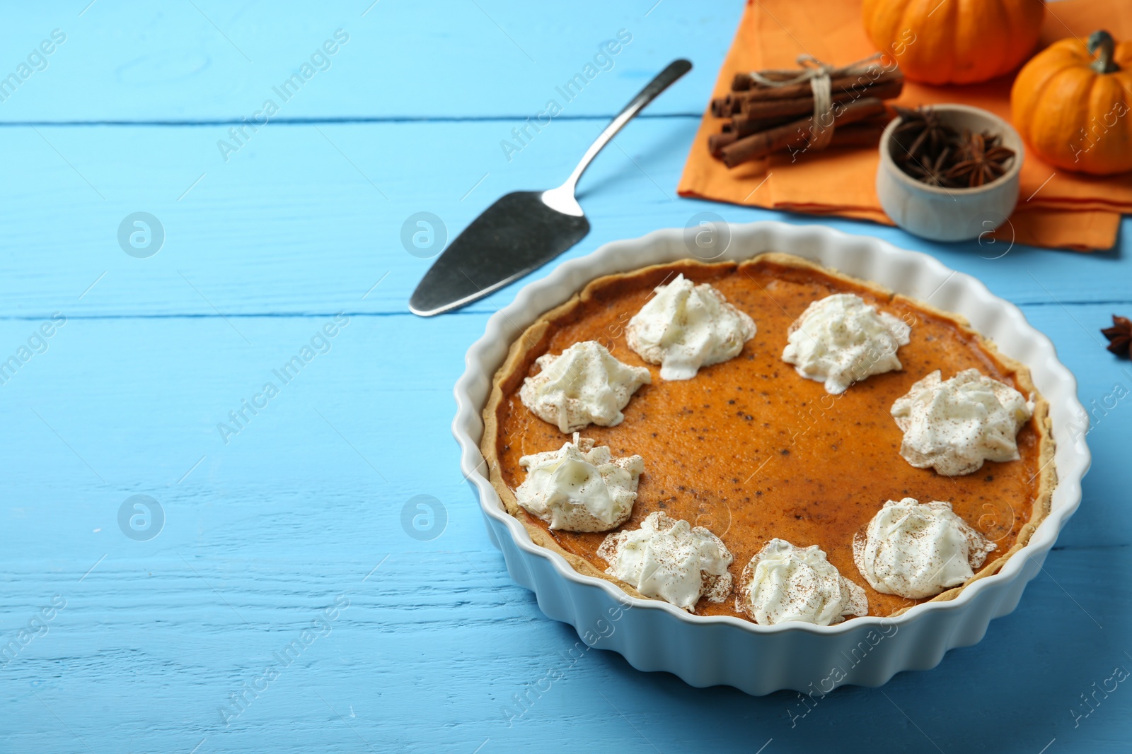 Photo of Delicious pumpkin pie with whipped cream on light blue wooden table, space for text