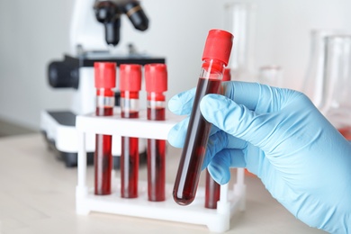 Scientist taking test tube with blood sample from rack at table, closeup. Laboratory analysis