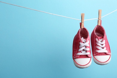 Cute small shoes hanging on washing line against color background, space for text. Baby accessories