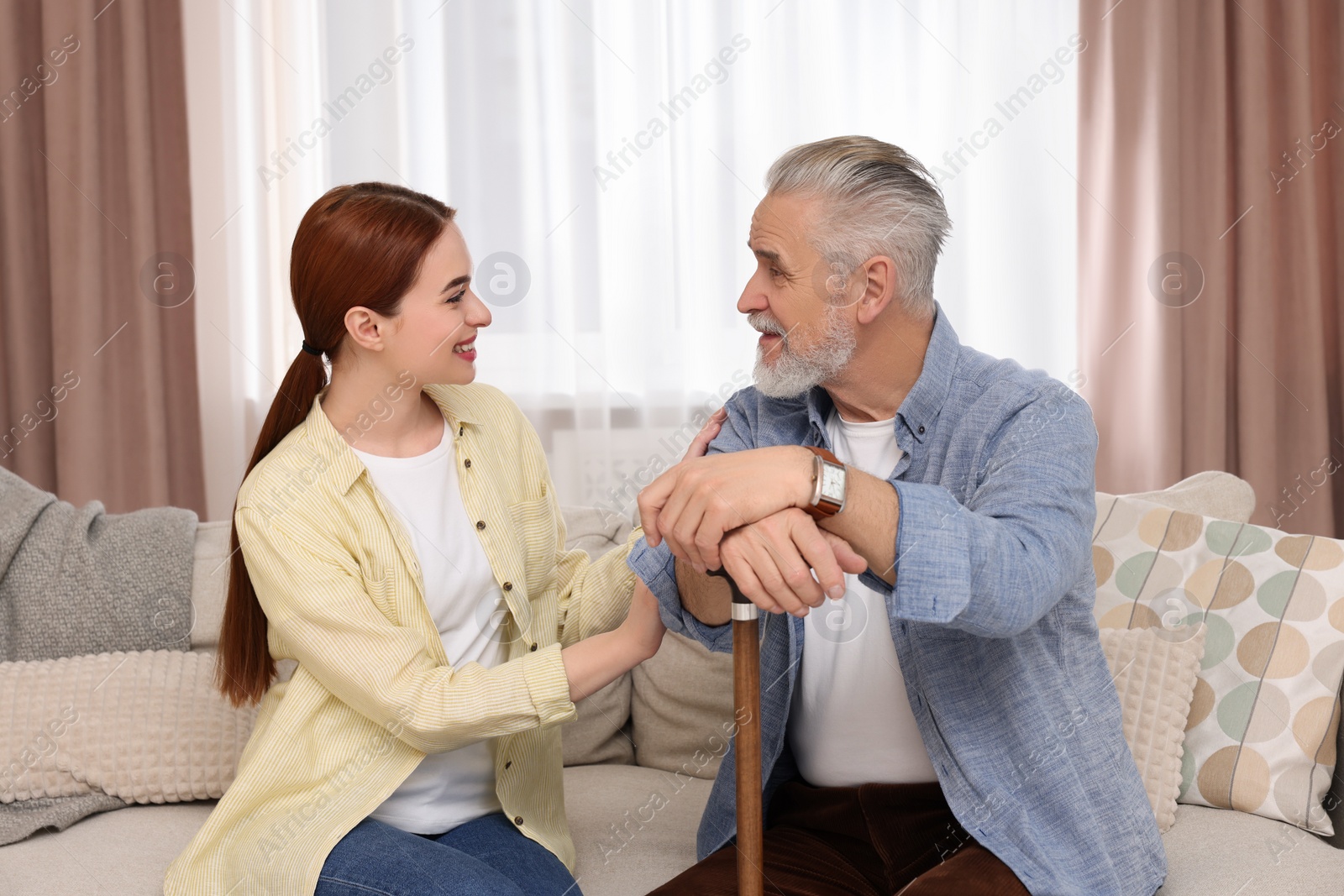 Photo of Caregiver and senior man with walking cane on sofa at home