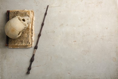 Photo of Magic wand, old book and human scull on light textured background, flat lay. Space for text