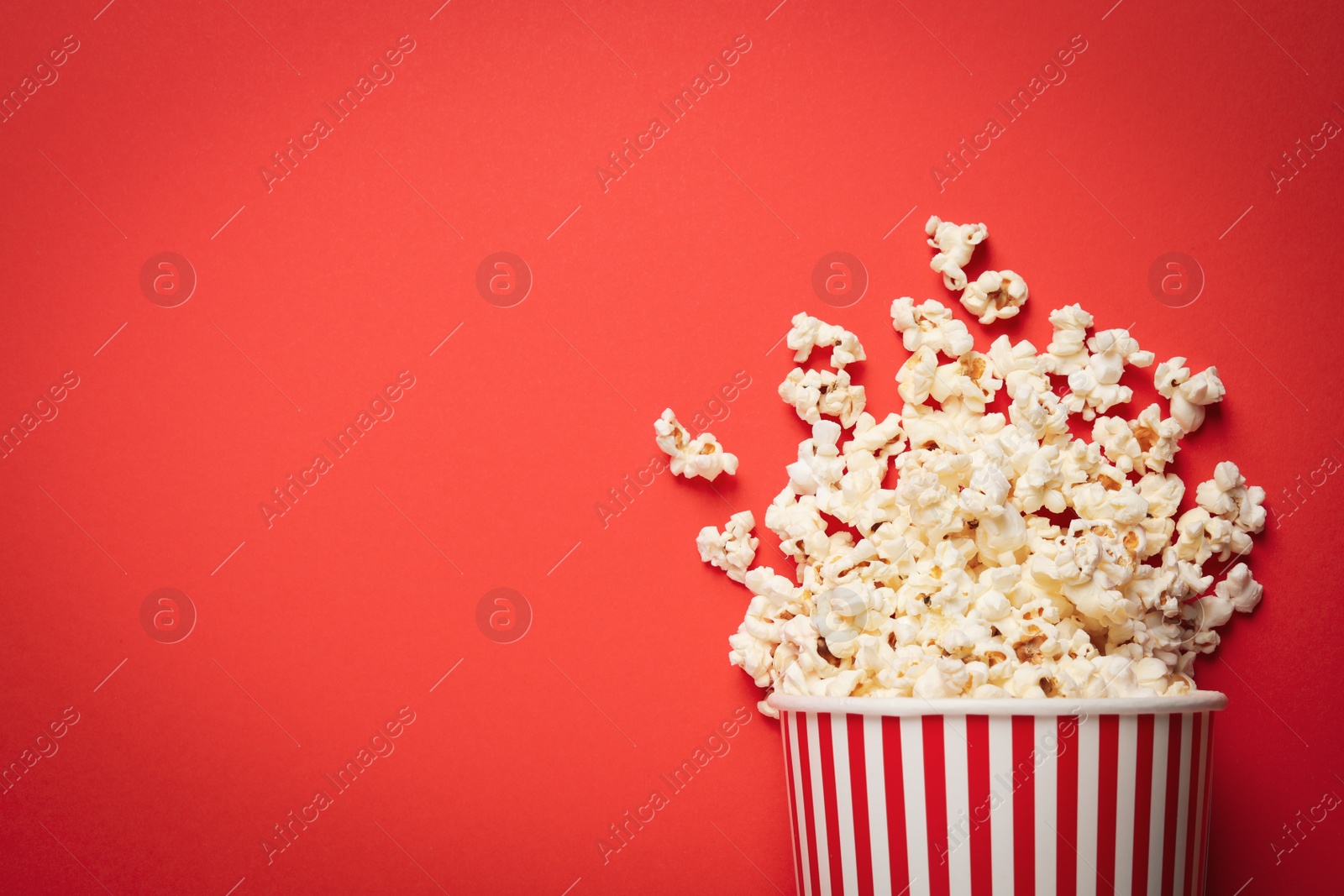 Photo of Overturned paper cup with delicious popcorn on red background, top view. Space for text