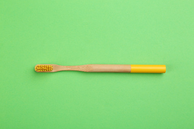Photo of Natural bamboo toothbrush on green background, top view