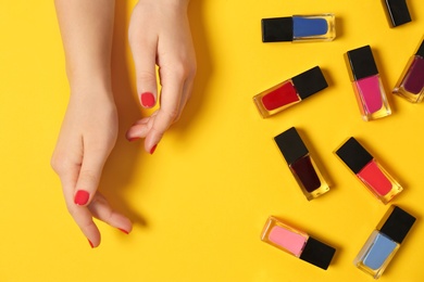 Woman with red manicure and nail polish bottles on color background, top view