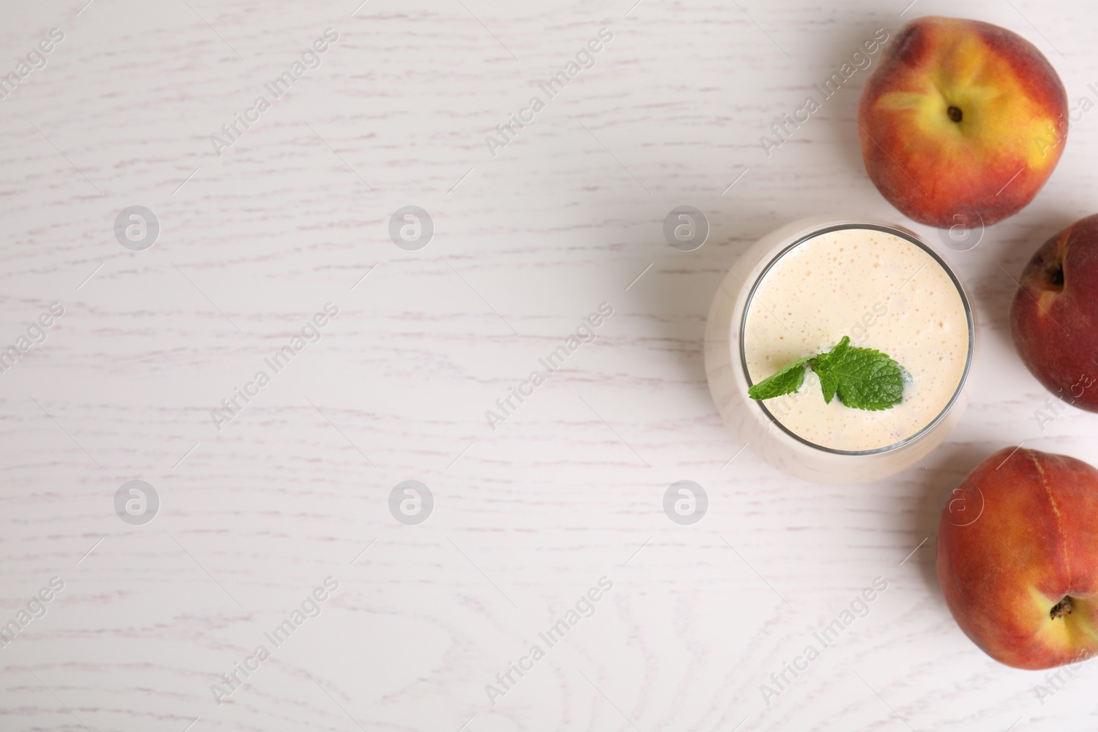 Photo of Tasty milk shake and fresh peaches on white wooden table, flat lay. Space for text