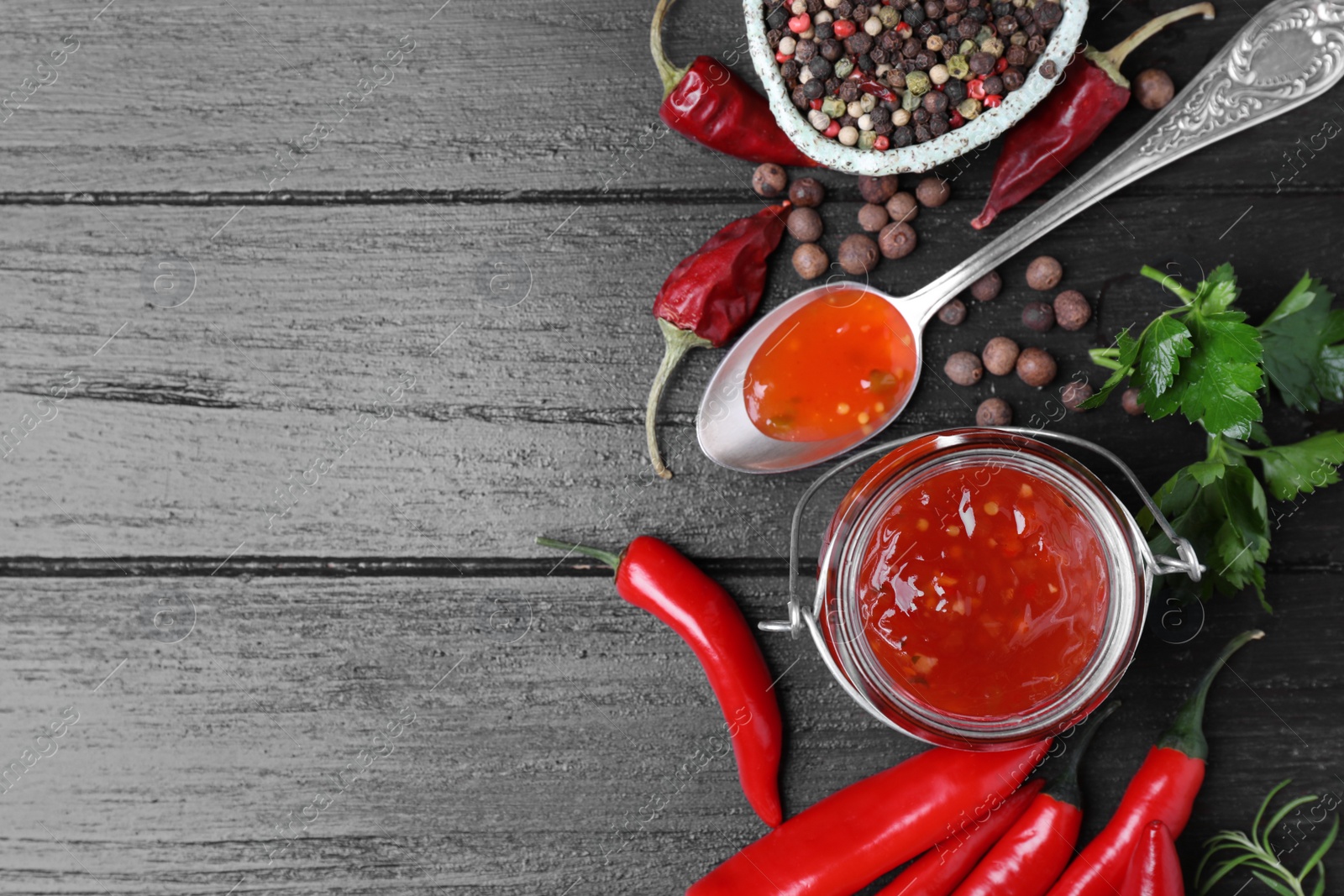 Photo of Jar and spoon of hot chili sauce with ingredients on wooden background, flat lay. Space for text