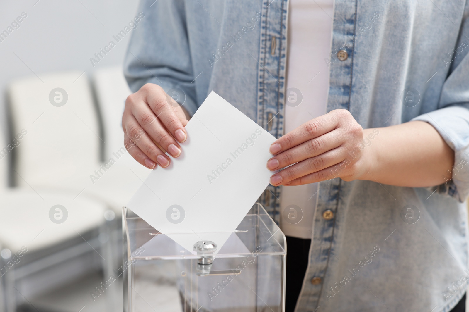 Photo of Woman putting her vote into ballot box on blurred background, closeup