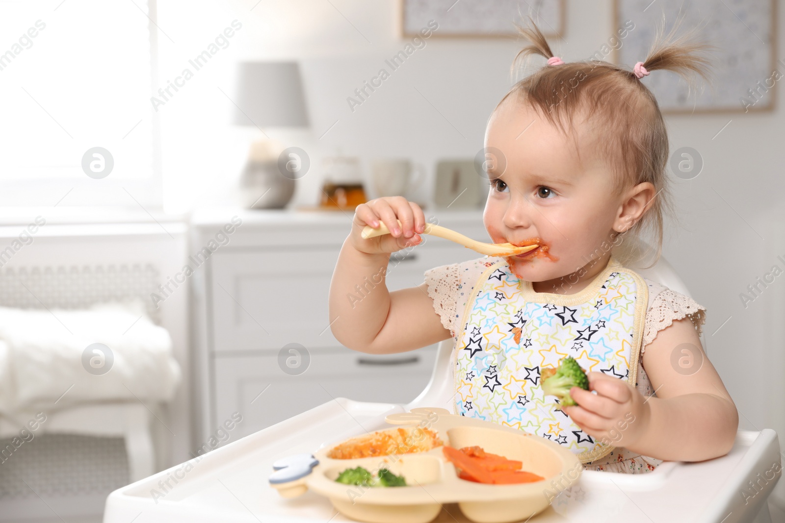 Photo of Cute little baby eating food in high chair at home